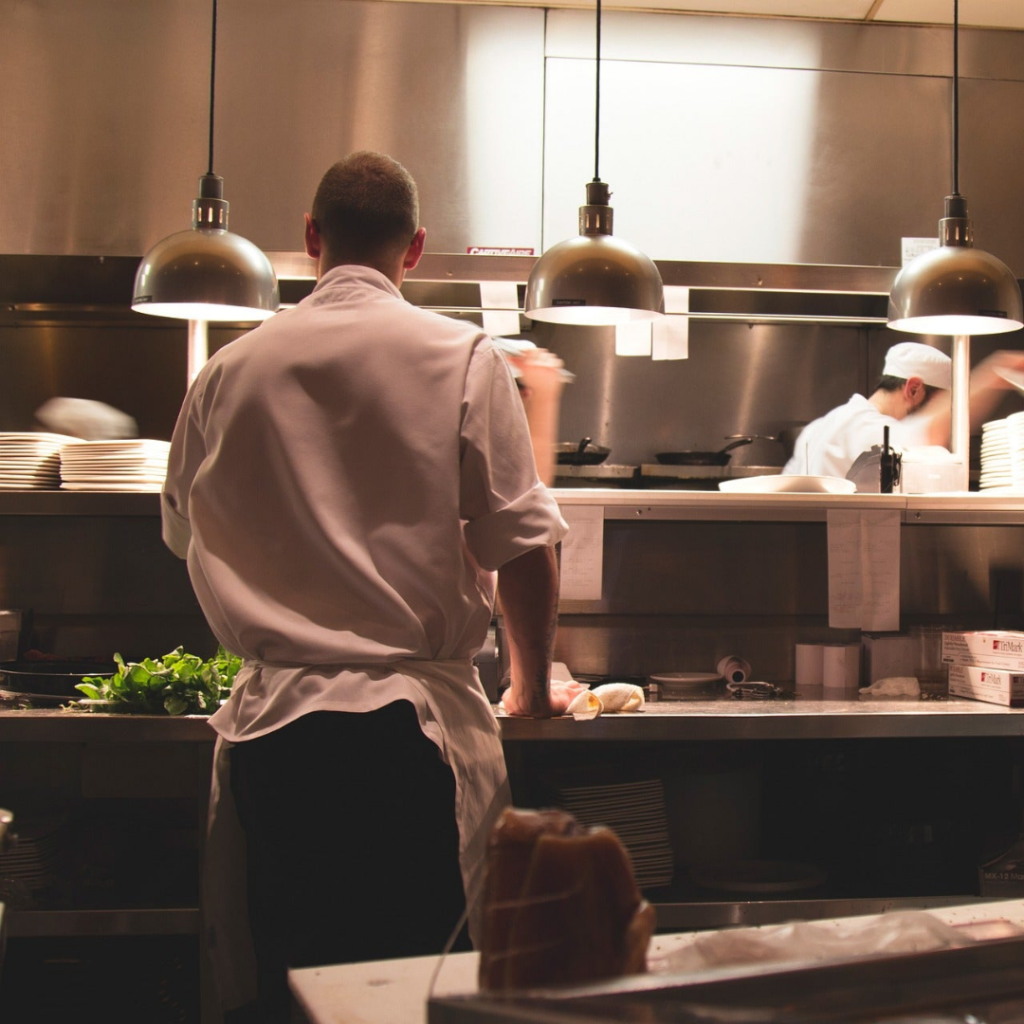 A man in white shirt and apron standing in kitchen.